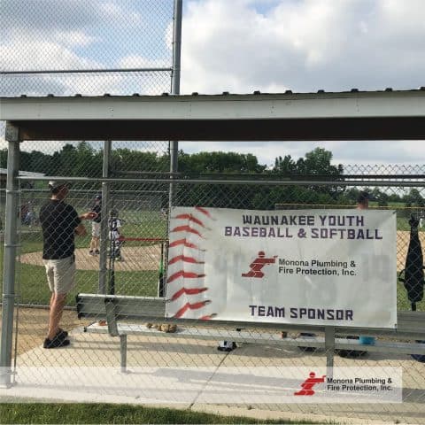 Monona Plumbing and Fire Protection banner at youth baseball field.