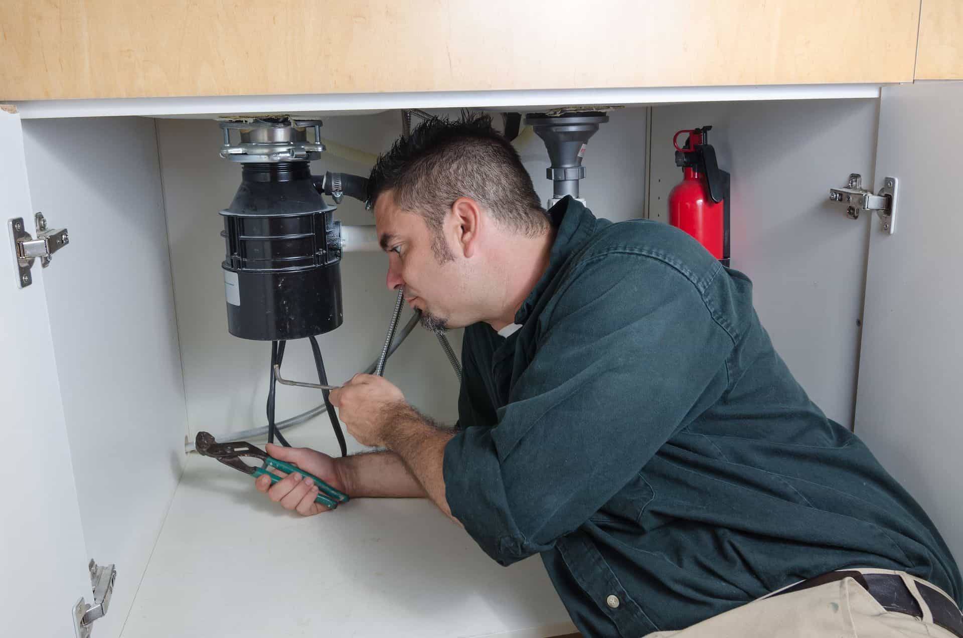 Plumber inspecting under sink for plumbing and fire protection systems.