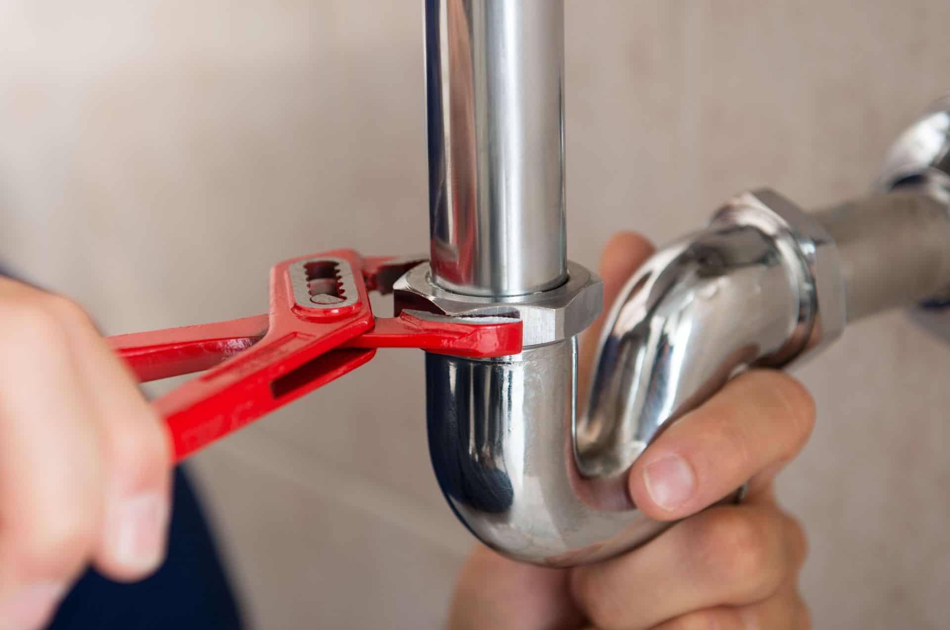 Plumber tightening a pipe fitting with a wrench for plumbing repair.