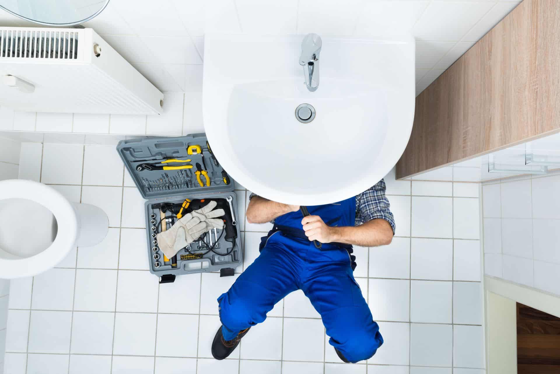 Plumber fixing bathroom sink with tools in a modern restroom.