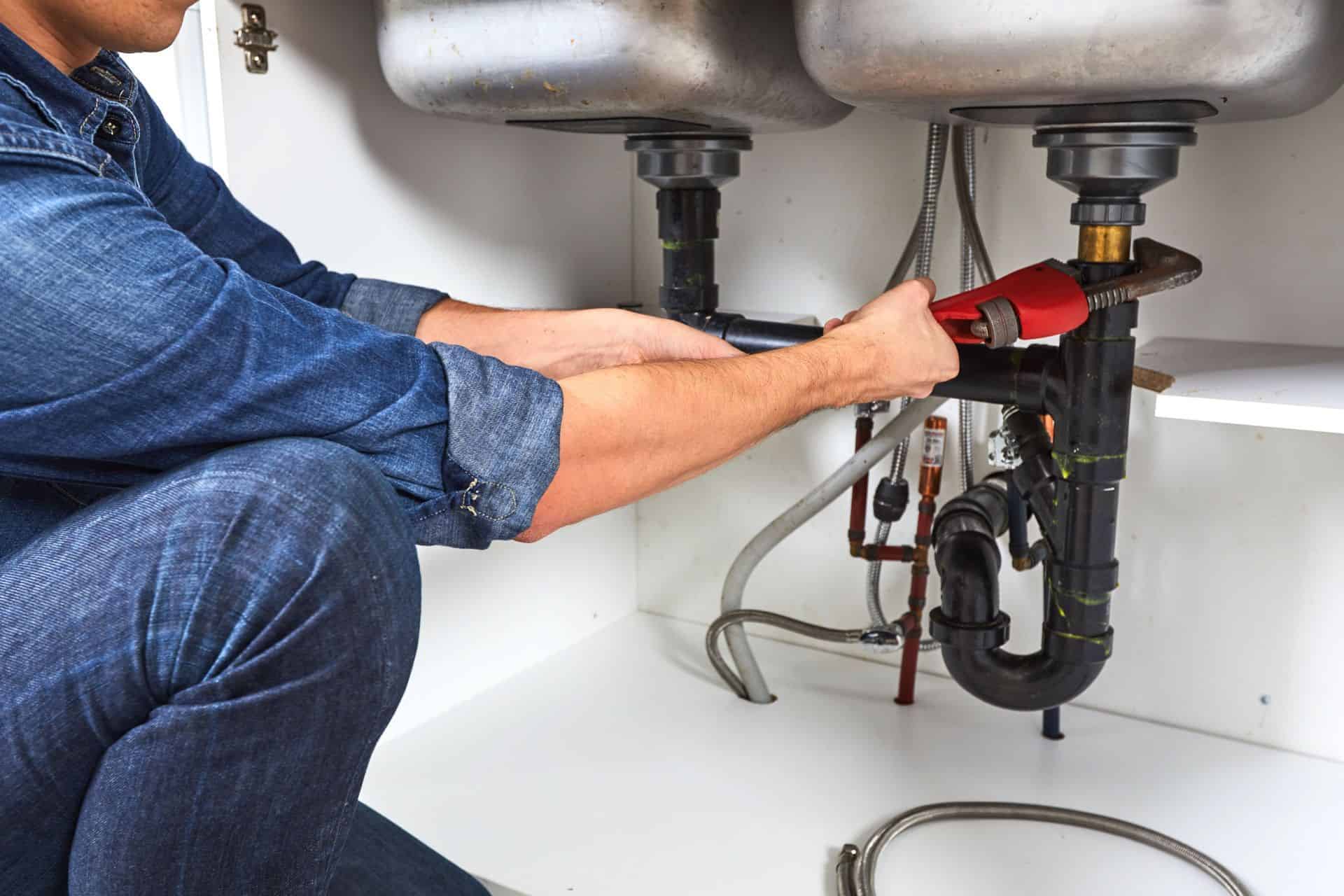 Plumber inspecting under double kitchen sinks with plumbing and fire protection systems.