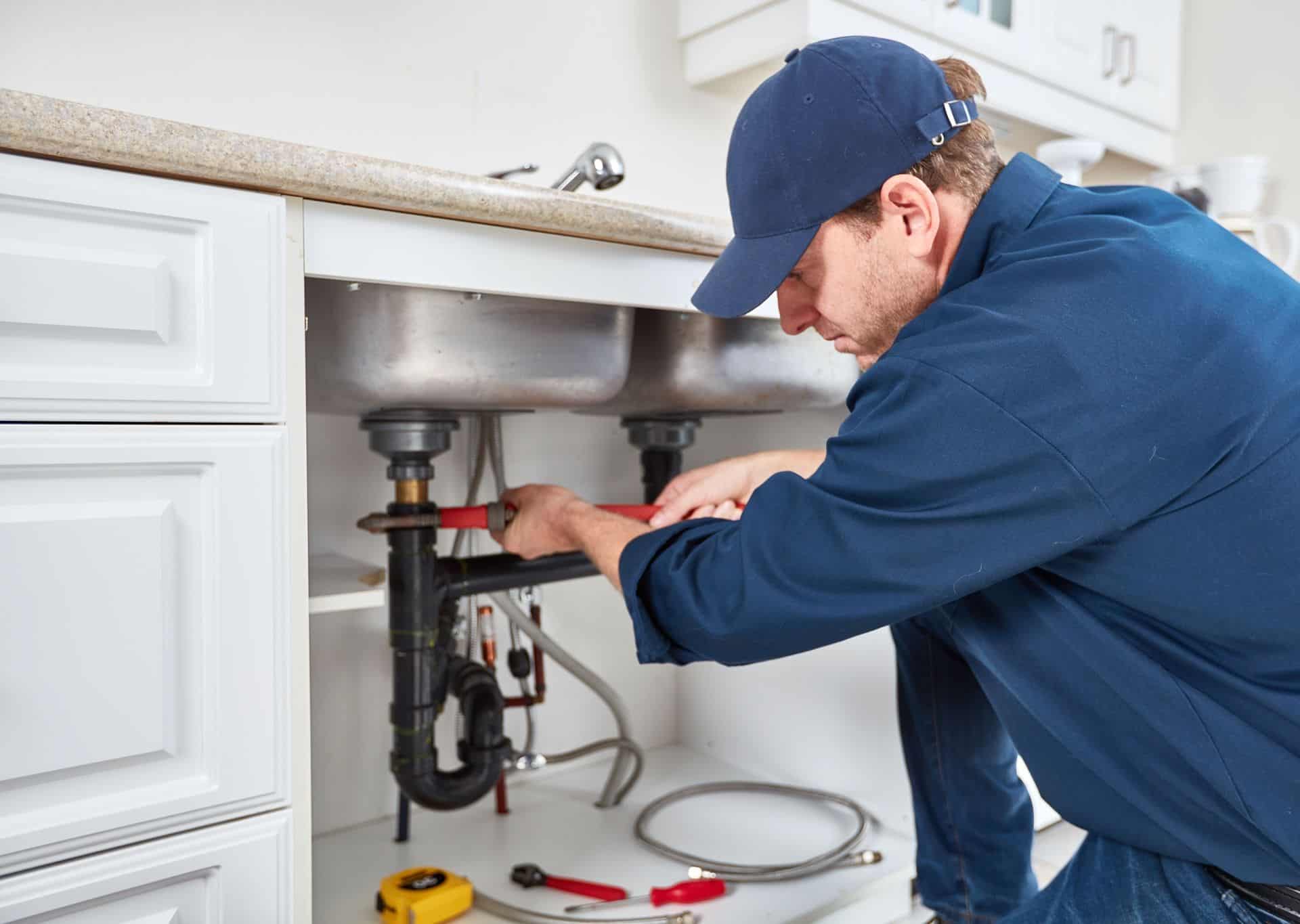 Plumber repairing under kitchen sink with plumbing and fire protection systems.