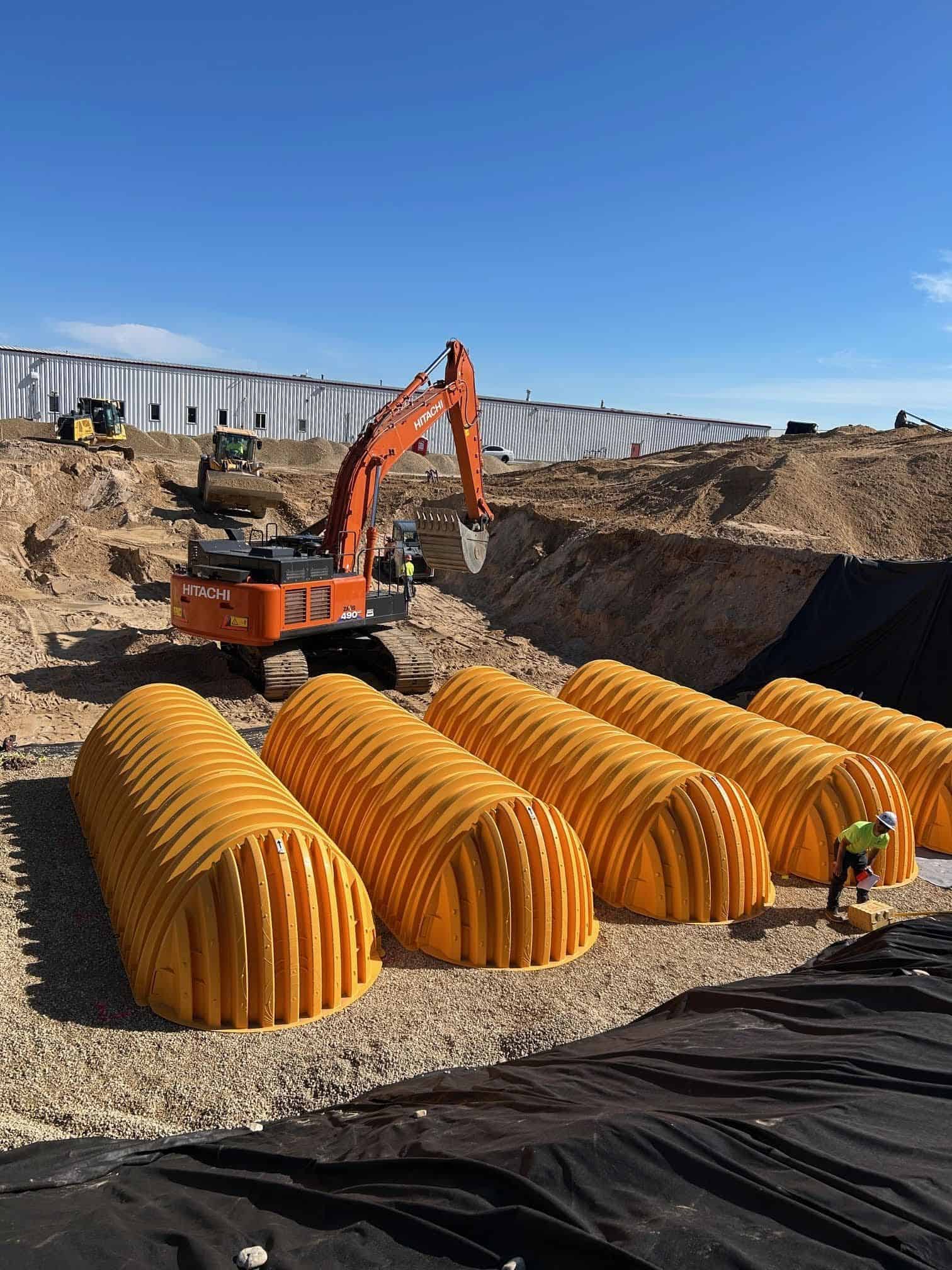 Installation of large orange underground plumbing and fire protection pipes at construction site.