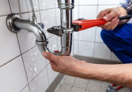 Technician repairing plumbing pipe with a wrench in a commercial building.