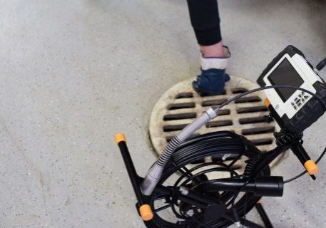 Plumbing technician inspecting drain cover with testing equipment in commercial space.