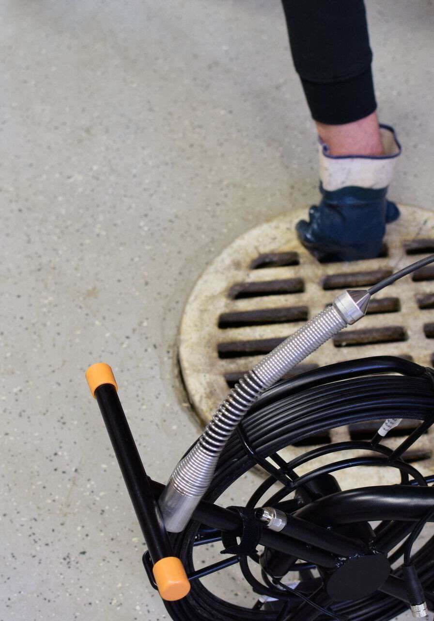Plumbing technician inspecting drain cover with testing equipment in commercial space.