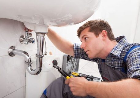 Plumber inspecting under sink for leaks and fire protection system maintenance.