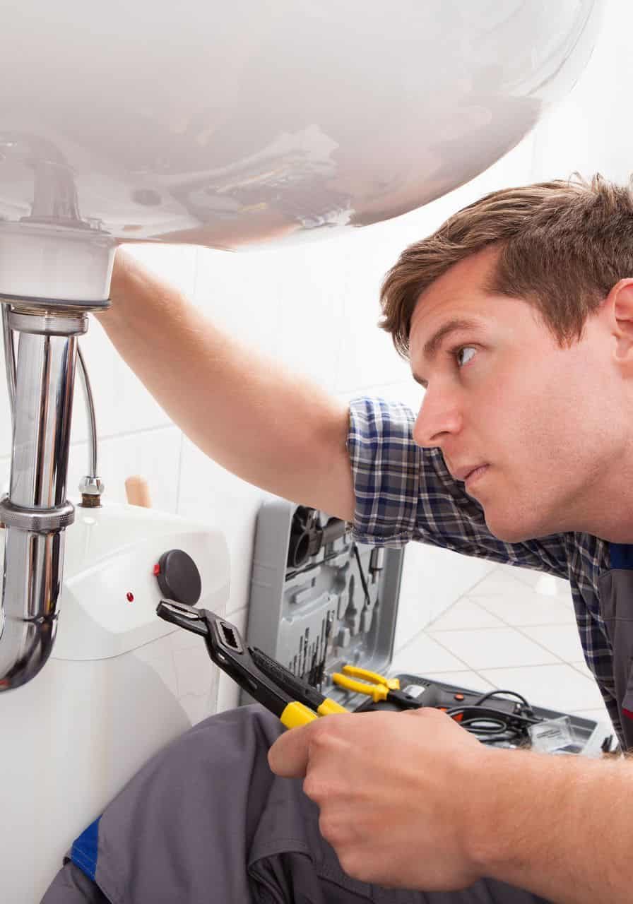 Plumber inspecting under sink for leaks and fire protection system maintenance.