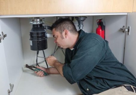 Plumber inspecting under sink for plumbing and fire protection systems.