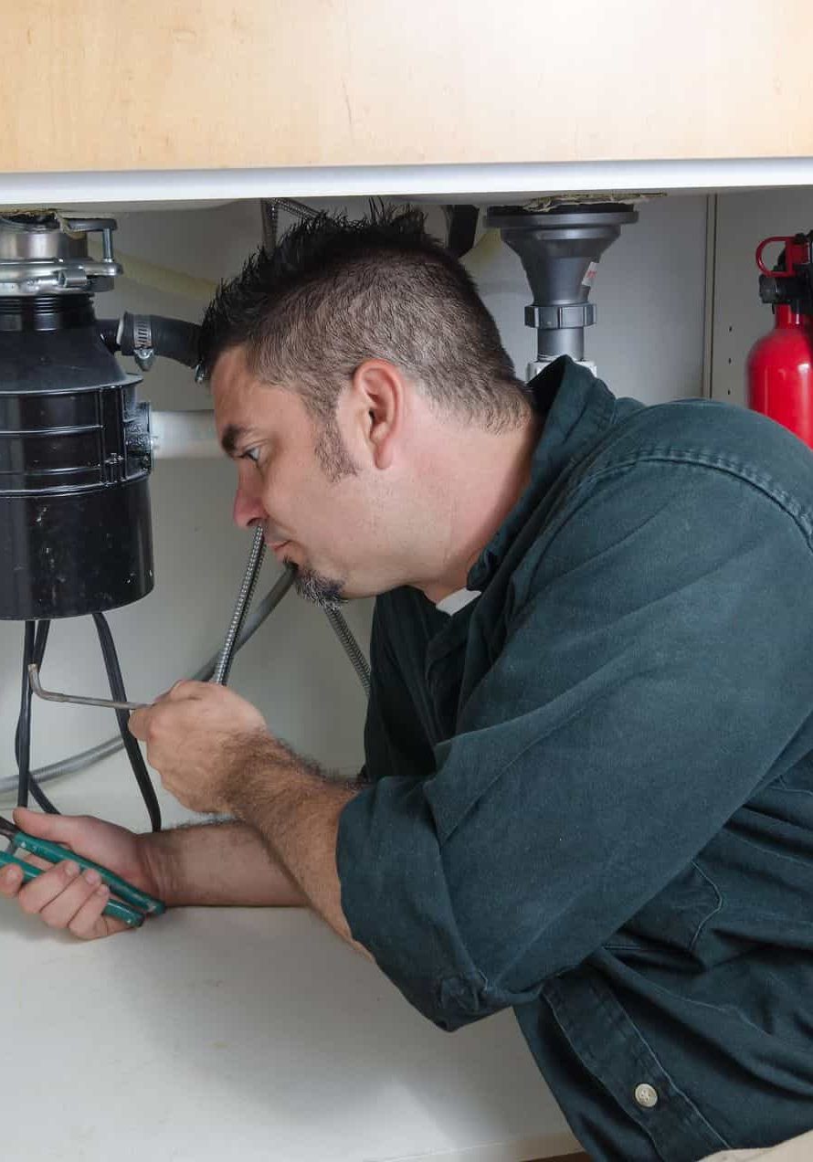Plumber inspecting under sink for plumbing and fire protection systems.