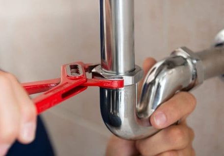 Plumber tightening a pipe fitting with a wrench for plumbing repair.