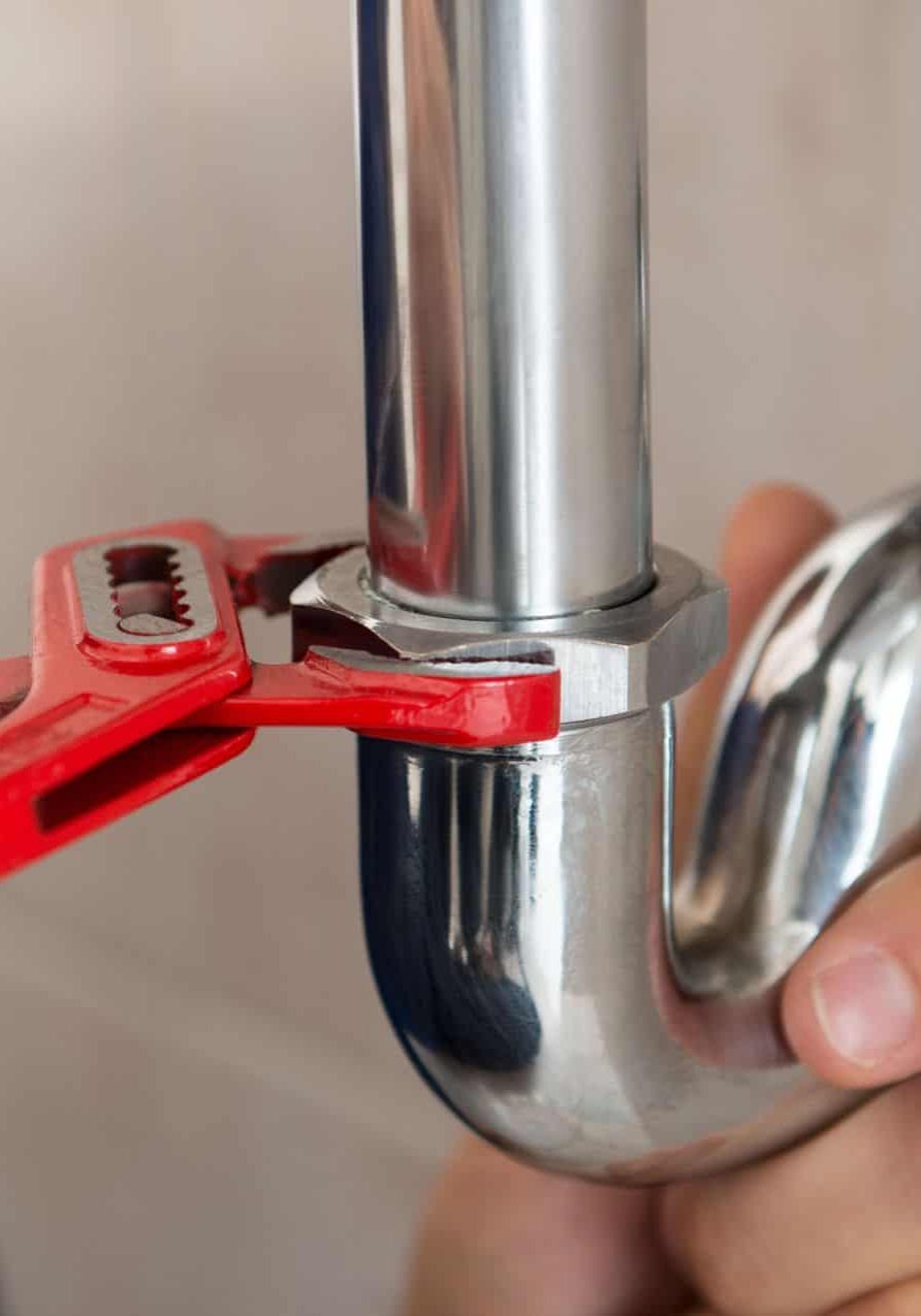 Plumber tightening a pipe fitting with a wrench for plumbing repair.