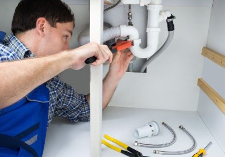 Plumber inspecting under sink for plumbing and fire protection systems.