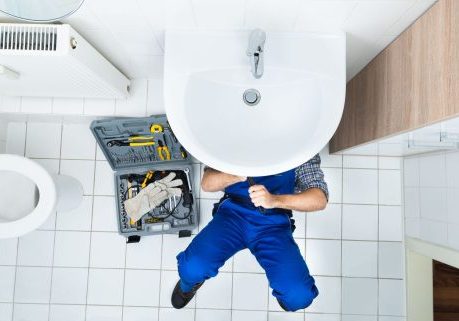 Plumber fixing bathroom sink with tools in a modern restroom.