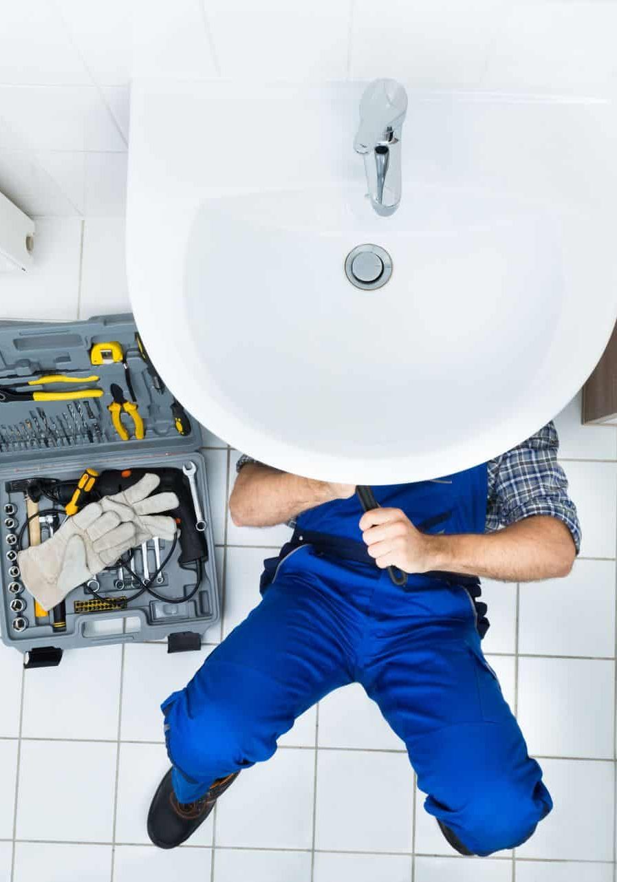 Plumber fixing bathroom sink with tools in a modern restroom.