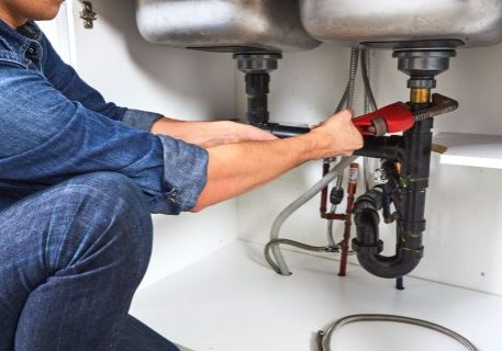 Plumber inspecting under double kitchen sinks with plumbing and fire protection systems.
