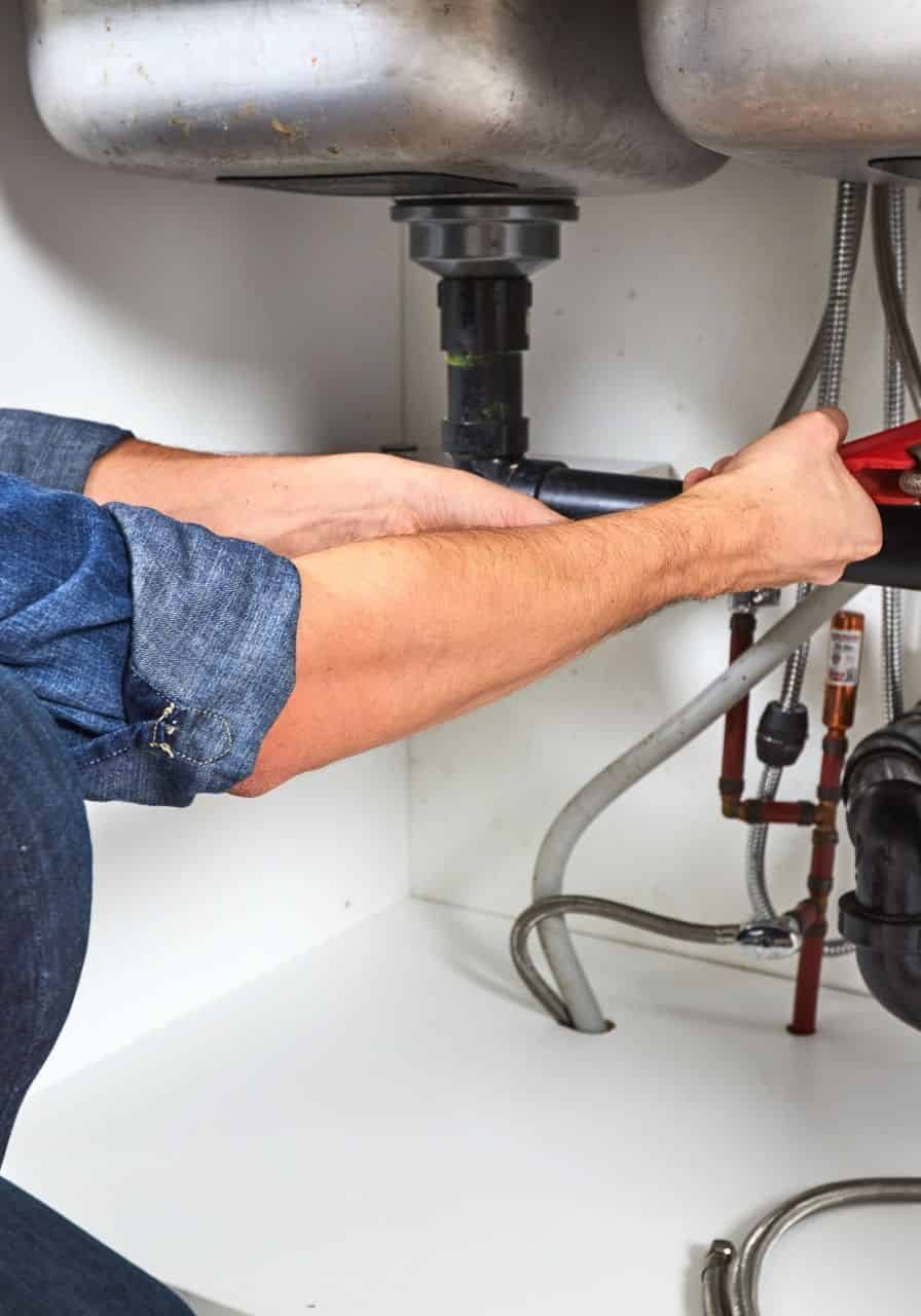 Plumber inspecting under double kitchen sinks with plumbing and fire protection systems.
