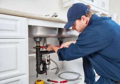Plumber repairing under kitchen sink with plumbing and fire protection systems.