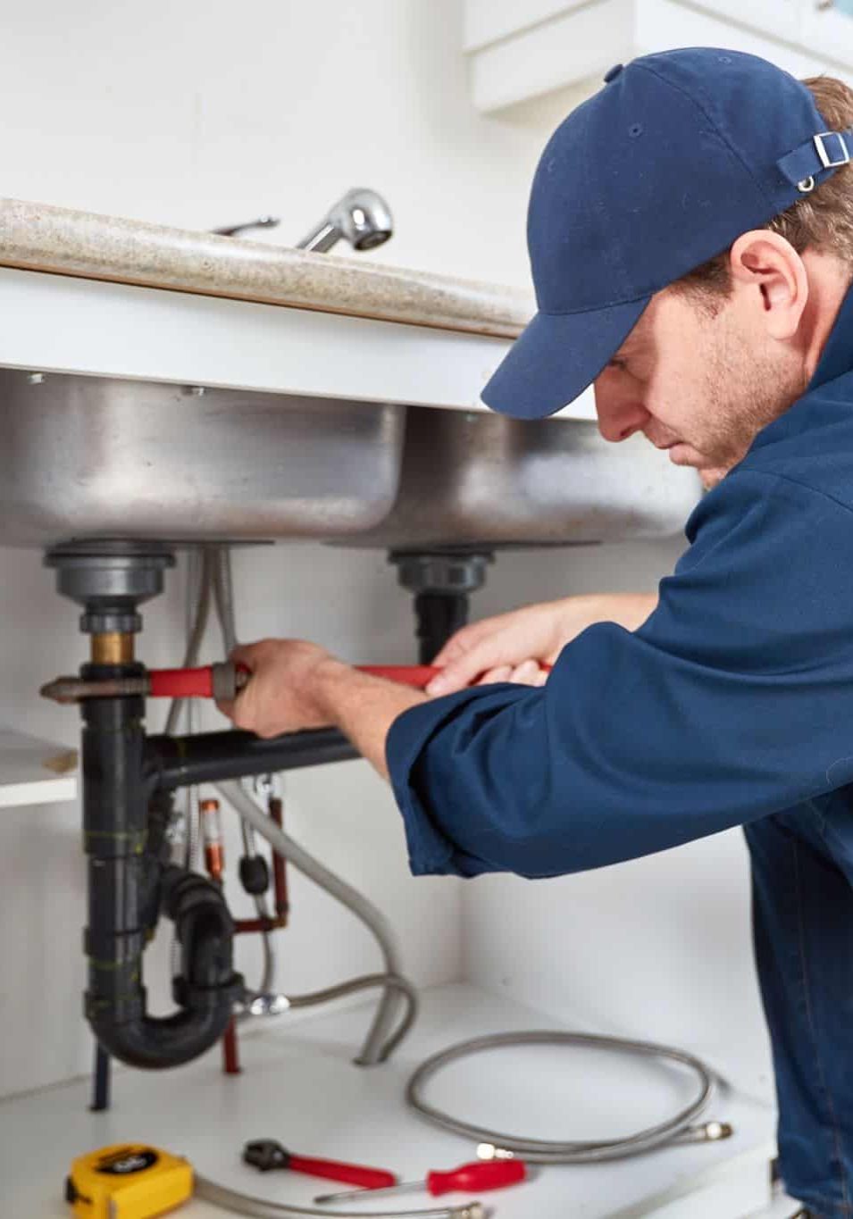 Plumber repairing under kitchen sink with plumbing and fire protection systems.