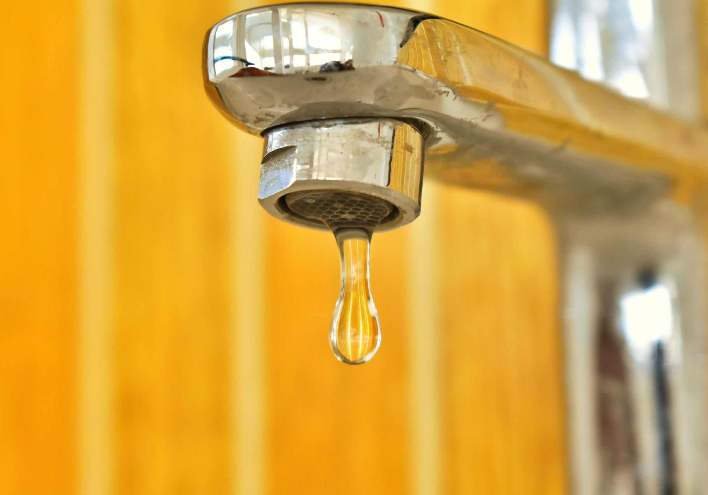 Plumbing faucet with water droplet, fire protection equipment in background.